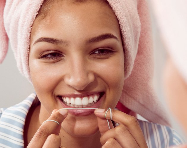 Woman flossing her pearly-white teeth and smiling while holding Cocofloss.